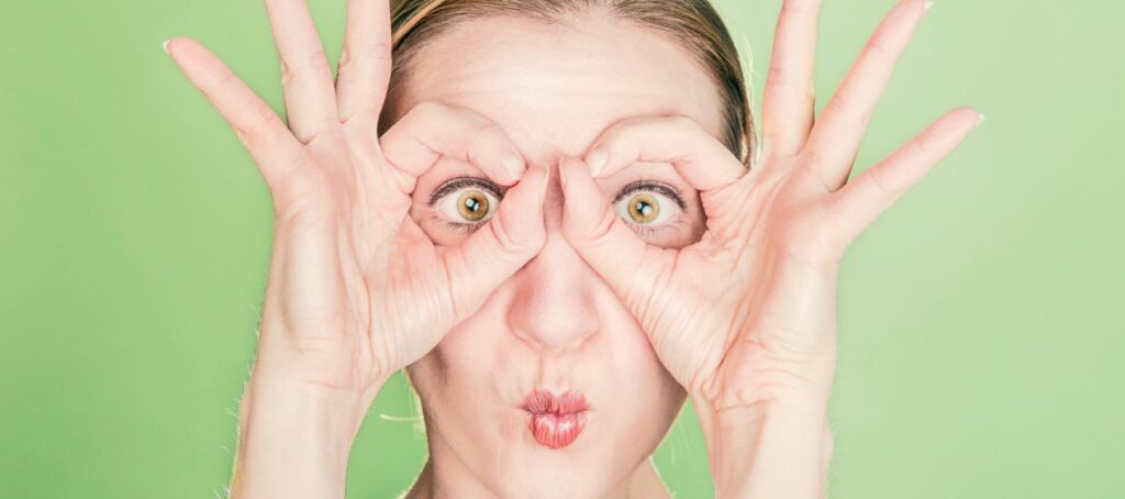 Donna che fa la forma degli occhiali con le mani intorno agli occhi su uno sfondo verde.